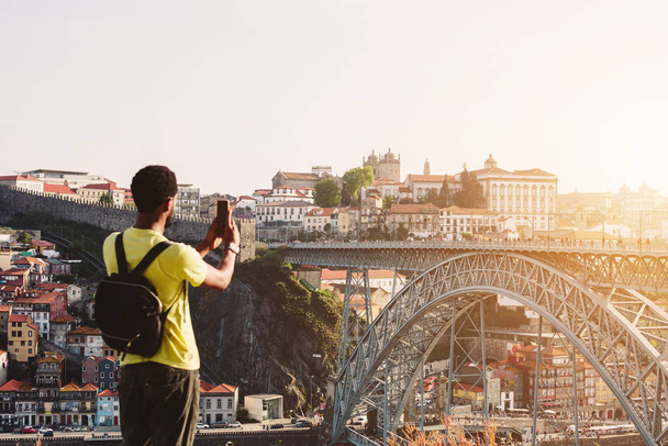 African man tourist take pictures on mobile phone of Ponte de Dom Luis I Bridge in Porto, Portugal - 写真・画像