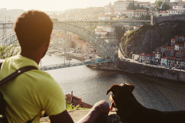 Traveler man with dog enjoying city view in Porto, famous iron bridge and Douro rive on background  - 写真・画像