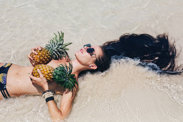 Belle femelle heureuse aux cheveux très longs tenant des ananas sur le rivage de la mer
 - Photo, image
