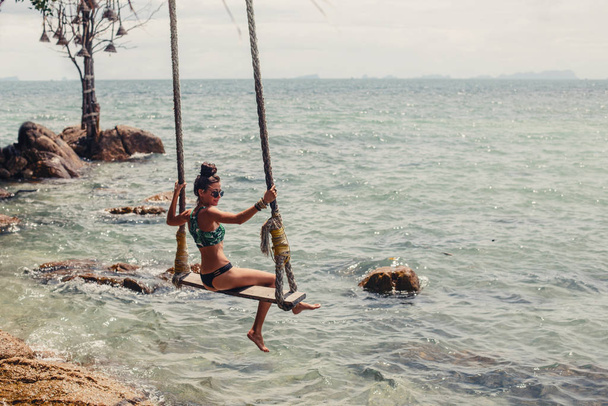Fashion female on swing on sea shore, tropical holidays - Foto, afbeelding