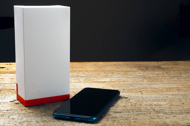 Новый смартфон рядом с пустым ящиком на деревянном столе
 - Фото, изображение