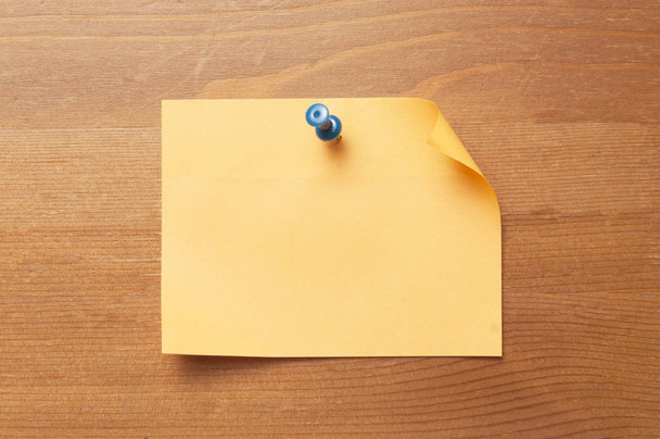 Oranje papieren memo bevestigd aan een houten tafel met een blauwe duimafdruk - Foto, afbeelding