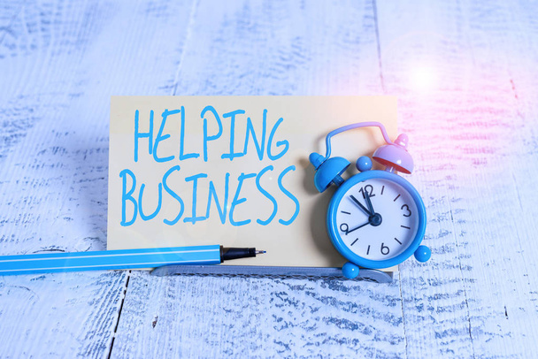 Handwriting text Helping Business. Concept meaning improving some measure of an enterprise s is success Mini blue alarm clock stand tilted above buffer wire in front of notepaper. - Photo, Image