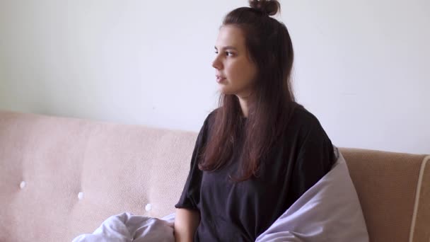 Mujer joven que sufre de dolor de estómago sentada en casa en el sofá
 - Imágenes, Vídeo