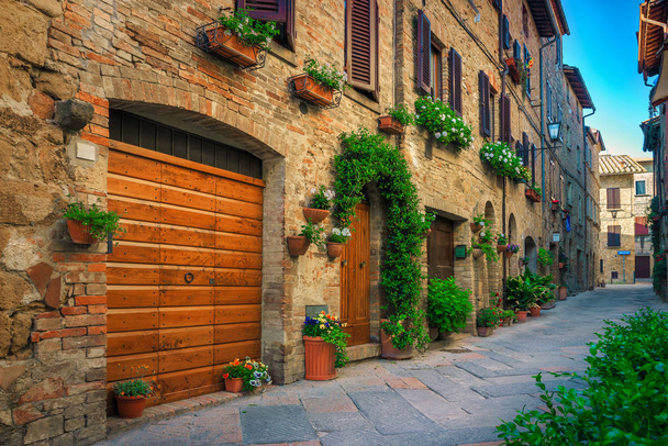 Cute narrow street decorated with flowers in Pienza, Tuscany, Italy - 写真・画像