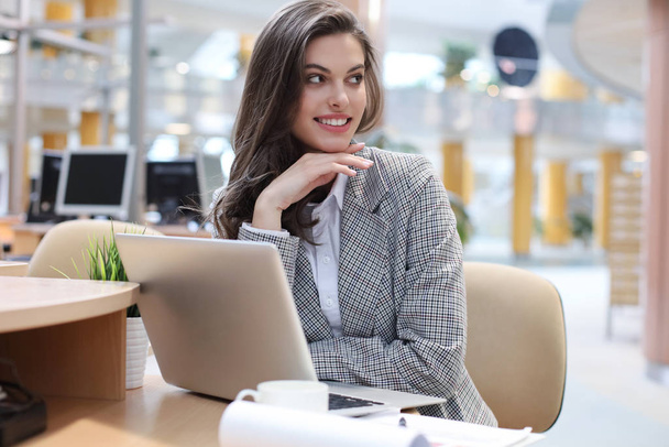 Portrait of a young brunette business woman using laptop at office. - Фото, зображення