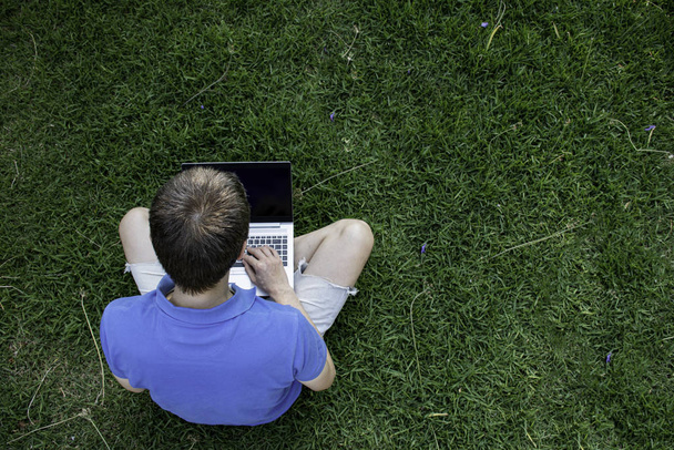 Человек, сидящий на зеленой траве в парке со своим ноутбуком. Работаю снаружи. Вид сверху. Пустое место для ввода текста
 - Фото, изображение