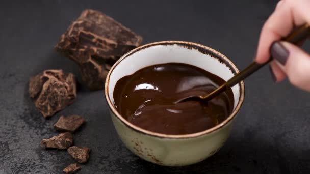 Liquid dark chocolate in bowl. Female hand mixing melted dark chocolate with spoon. Chocolate fondue - 映像、動画