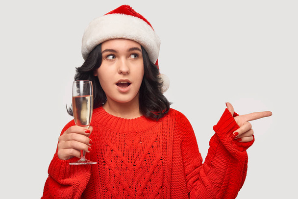 Tyttö punainen pusero ja Santa hattu pitämällä lasi samppanjaa ja osoittaa kopioi tilaa
 - Valokuva, kuva