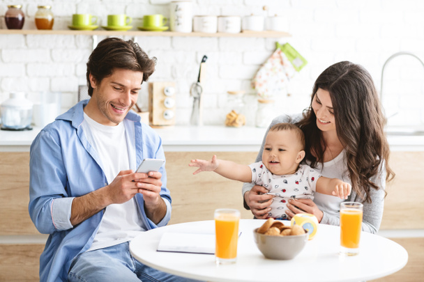 Millennial man texting on phone, dining with wife and baby - Photo, Image