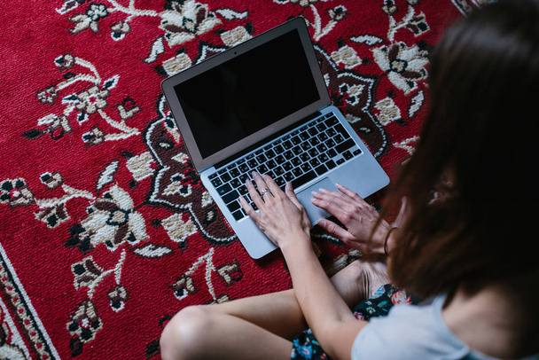 Young female freelancer sitting with laptop computer on the red carpet. Home work space and free travel concept - Photo, image