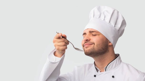 Piacevole chef uomo degustazione cibo in piedi su sfondo bianco, Panorama
 - Foto, immagini