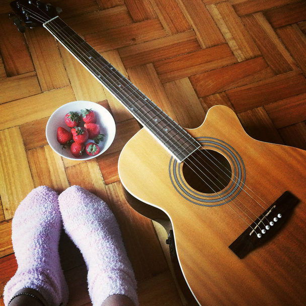  guitar, strawberries, female feet in warm socks on parquet floor. Mobile photo - Foto, Bild
