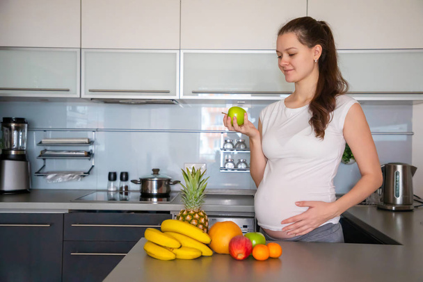 Pregnant woman and different tropical fruits in home kitchen - Foto, Bild