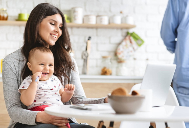SuMillennial mère travaillant sur ordinateur portable avec bébé à la cuisine
 - Photo, image