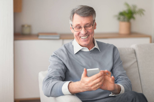 Senior Man Using Cellphone Browsing Internet Sitting On Sofa Indoor - Valokuva, kuva