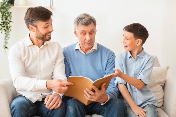 Дідусь читає книгу зі зрілим сином і онуком вдома
 - Фото, зображення