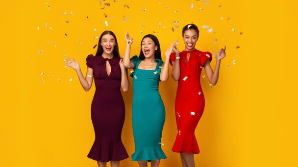 Kolme osapuolta tytöt seisoo Falling Silver Confettin alla, keltainen tausta
 - Valokuva, kuva