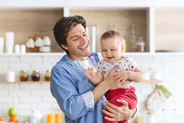 Cheerful daddy embracing his adorable baby at kitchen - Valokuva, kuva