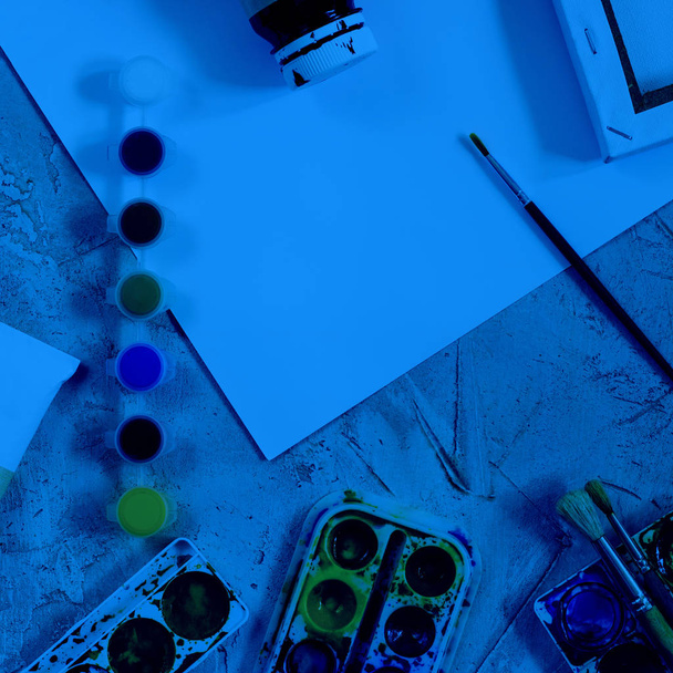 Flatlay with bright paints in small round containers and many palettes, brush and white sheet of paper on grey cement backcground, Workspace, Mess, Classic, blue monochrome, trend 2020. Back to school - Fotoğraf, Görsel
