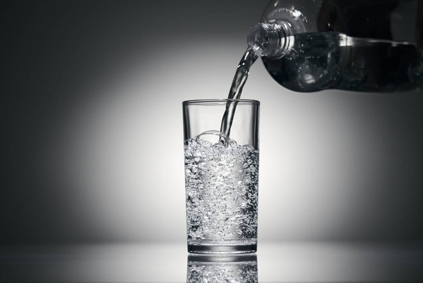 Wlewanie wody gazowanej do szklanki na ciemnym tle - Zdjęcie, obraz