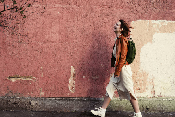 Young female wearing little backpack walking outdoor in city opposite coloured wall - Fotoğraf, Görsel