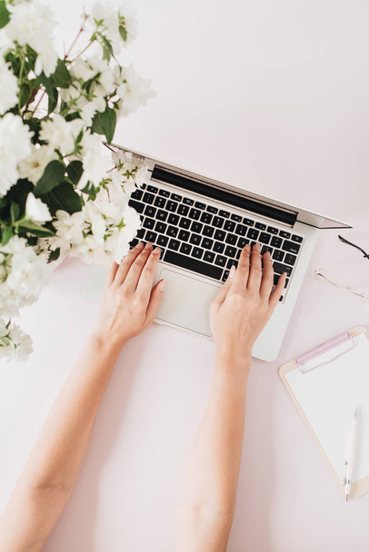 Woman works on laptop. Freelancer co-working office desk workspace with flowers bouquet and stationery on white table. Flat lay, top view business hero header background. - Fotó, kép