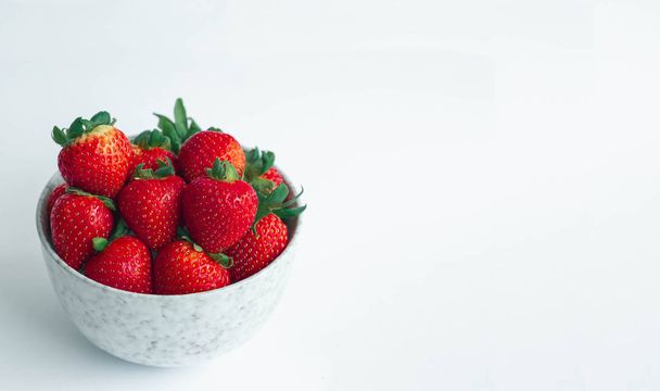 Fresas frescas con cabeza de hoja verde en un cuenco de porcelana de mármol blanco sobre fondo blanco con espacio para copiar, para pancarta
 - Foto, Imagen