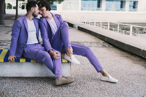 Romantic gay couple wearing purple color suits seating outdoor on seafront together, Happy Wedding walking day - Fotografie, Obrázek