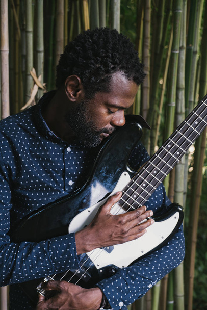 Portrait of African musician bass guitar player outdoors, natural bamboo background - Photo, Image