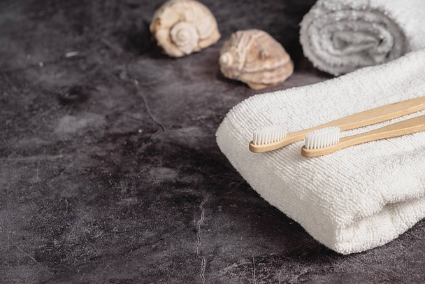 Dental care and Eco friendly and reuse concept. Two eco natural bamboo toothbrushes, seashell, white towel on grey background. Sustainable lifestyle and zero waste home. Copy space - Photo, Image