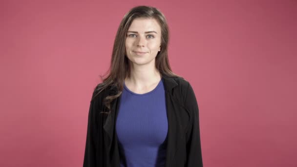 Happy young woman smiling and standing against pink background. - Video