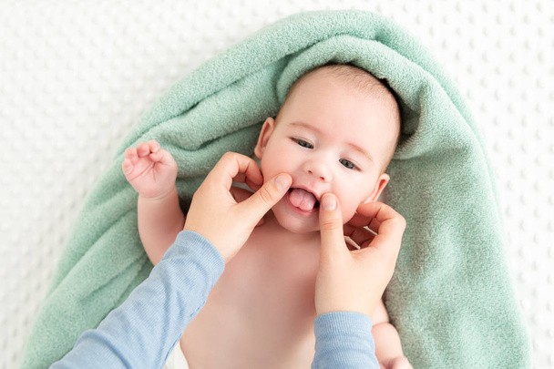 Baby face massage background. Mother gently stroking baby boy face with both hands. Close up cropped shot. Baby smiling during face massage. - 写真・画像