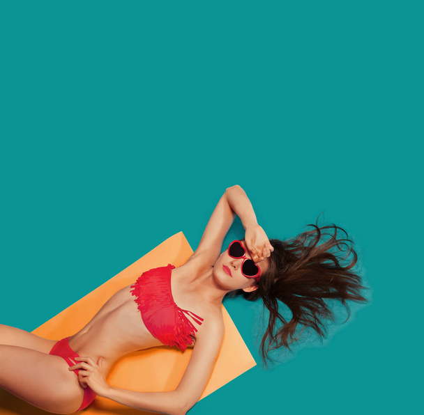 Summer Vacation abstract concept. Colorful studio portrait of young Fashion Woman in red swimsuit and sunglasses. Isolated on Blue background, orange mat - Fotografie, Obrázek
