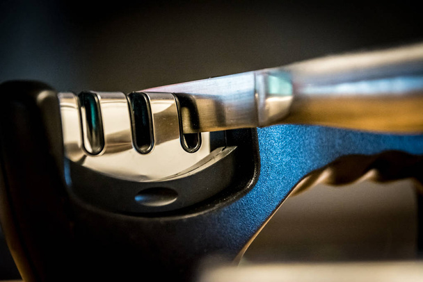Close-up and detail of a knife in a knife sharpener kitchen tool. Metal and chrome. Blurred background. - Φωτογραφία, εικόνα