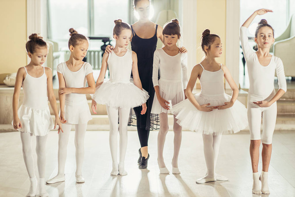 young woman ballet teacher and kids stand on tiptoes in studio - 写真・画像