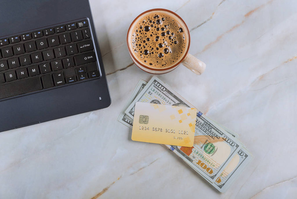 Mesa de oficina con billetes de cien dólares, computadora con tarjeta de crédito y taza de café
 - Foto, Imagen