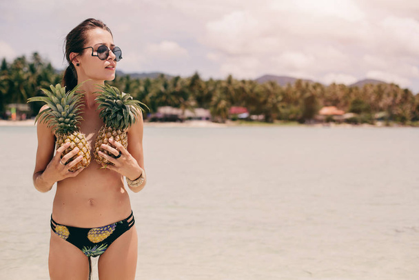 Beautiful happy female with very long hair holding pineapples on sea shore - Photo, image