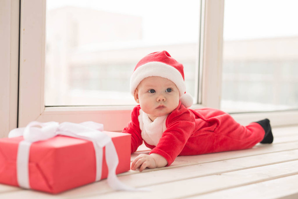 Piękne maleństwo świętuje święta. Noworoczne wakacje. Dziecko w stroju świątecznym i w czapce Mikołaja - Zdjęcie, obraz