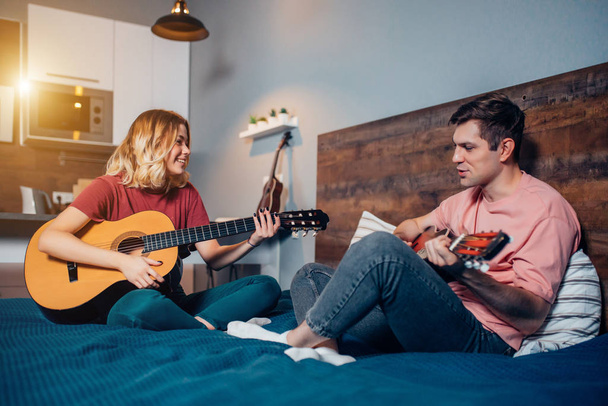 Güzel kız ve yakışıklı adam evde birlikte gitar çalıyorlar. - Fotoğraf, Görsel