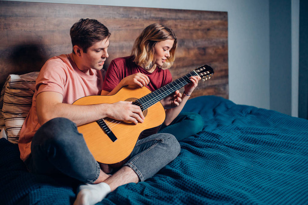 Beautiful girl and handsome guy playing guitar together at home - Foto, Bild