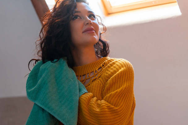 Close up of attractive brunette woman in yellow sweater drying curly hair with blue towel. Curly method of hair care. - Foto, immagini