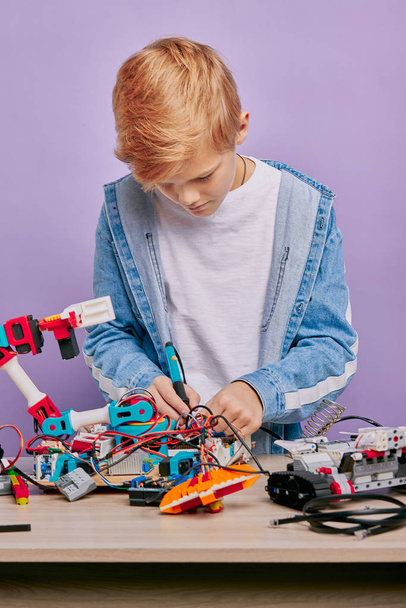 smart clever kid boy in casual wear assemble robots - Foto, afbeelding