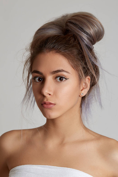 Closeup portrait of a young beautiful girl on a light background. A young girl smiles and enjoys life. Girl with a bun at her head. - Foto, Bild