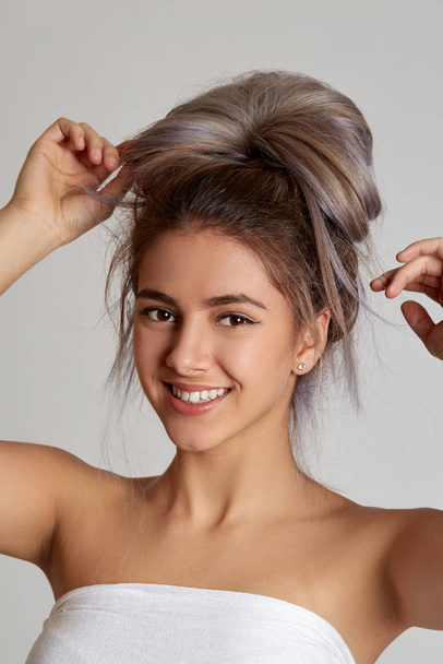 Closeup portrait of a young beautiful girl on a light background. A young girl smiles and enjoys life. Girl with a bun at her head. - Фото, изображение