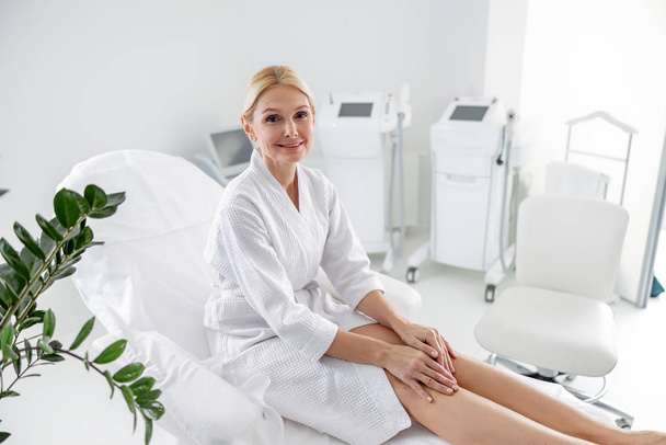 Smiling adult woman sitting in bathrobe at spa center - Photo, image