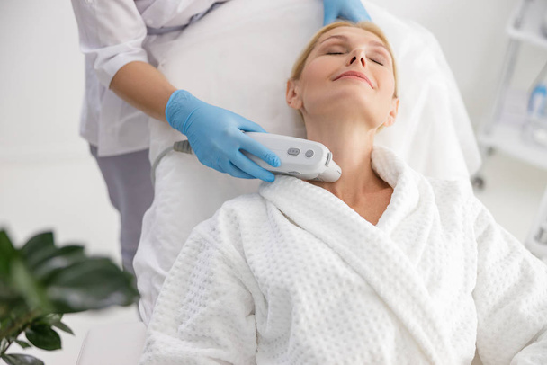 Female specialist is using skin lifting apparatus - Foto, afbeelding