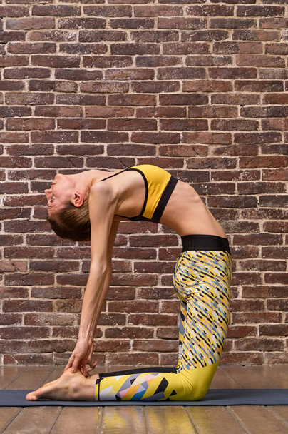 Beautiful woman with slender body doing yoga in on a brick wall  - Photo, Image