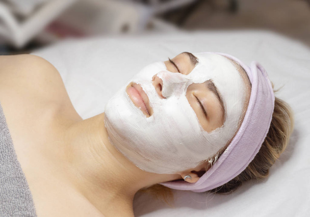 Young woman lies with a white clay mask applied to her face in a beauty salon - Foto, Imagem