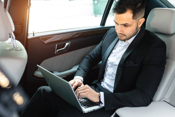 bearded young man working on laptop while driving car - Photo, Image